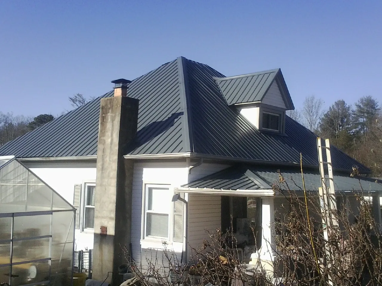 Dark blue standing seam metal roof on a white farmhouse with dormer — Slate & Tile Roof Repair by Roofing Brothers in Savona