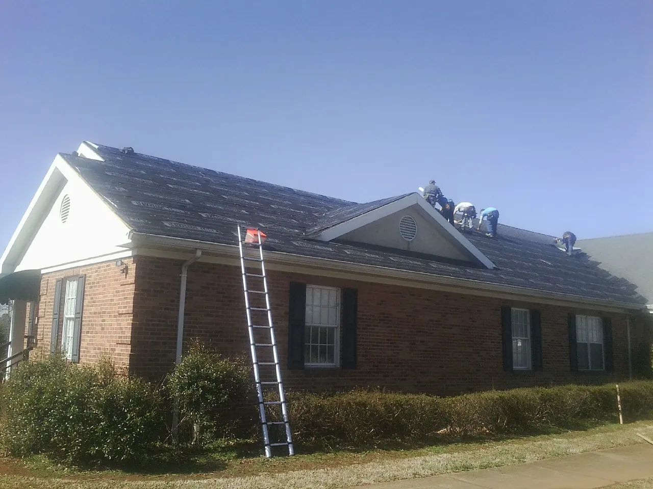 Crew tearing shingles off a brick ranch roof with a ladder set — Emergency Roof Repair work by our crew in Savona