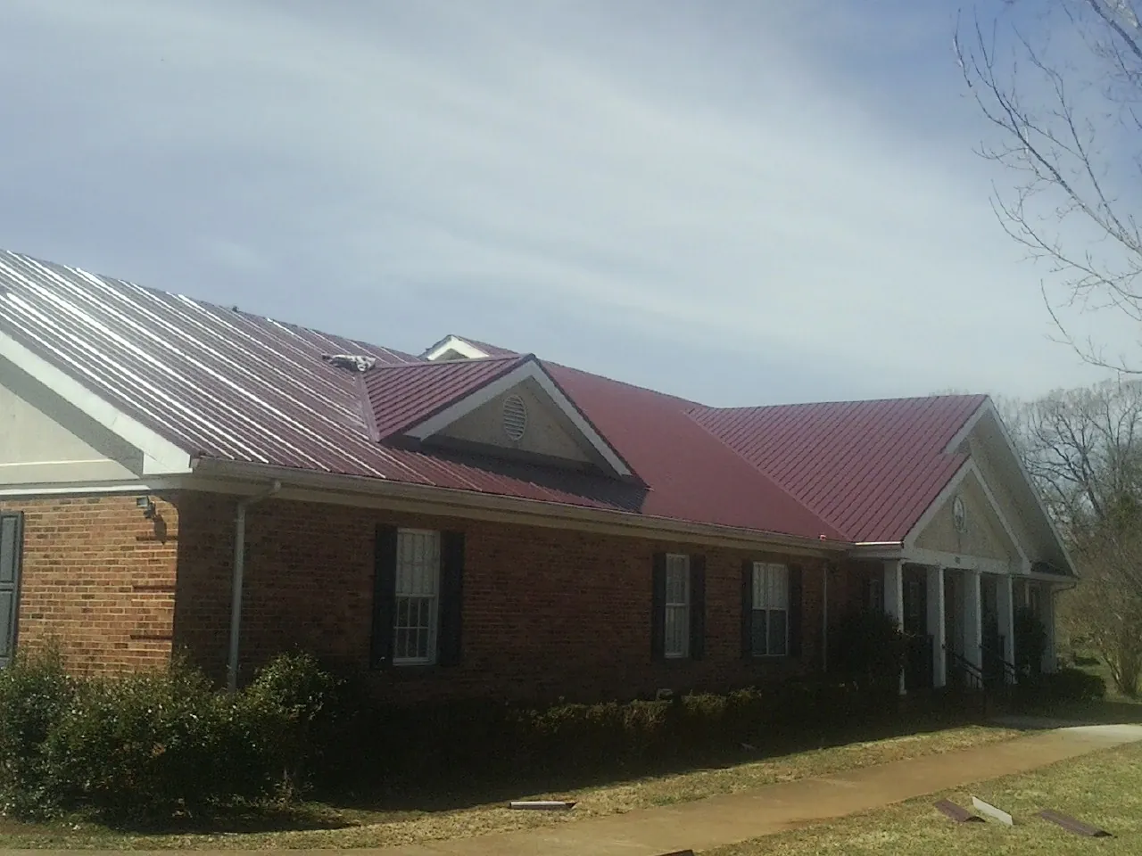 Red metal roof with gabled entries on a long brick building, from a Hail Damage Roof Repair job in Savona