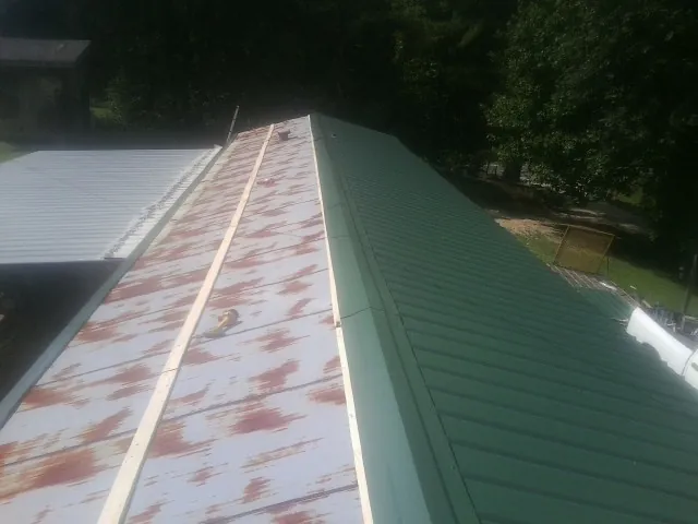 Old rusted panels beside newly installed green metal roofing — Wind Damage Roof Repair by Roofing Brothers in Savona