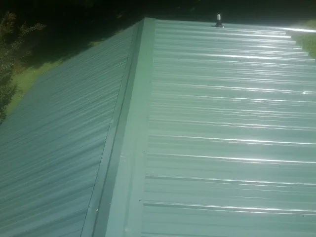 New green metal panels meeting at the ridge of a roof — Flat Roof Repair work by our crew in Savona