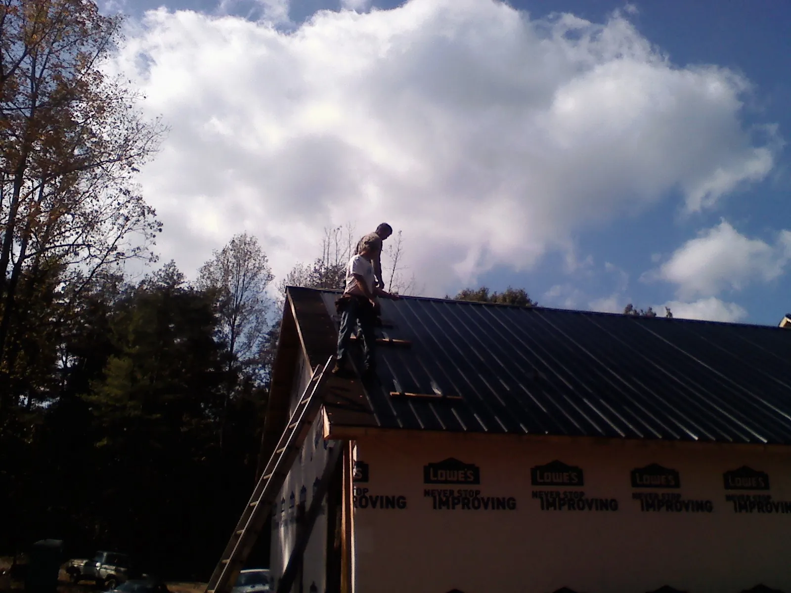 Roofer fastening dark metal panels high against a cloudy sky, from a Roof Inspection job in Savona