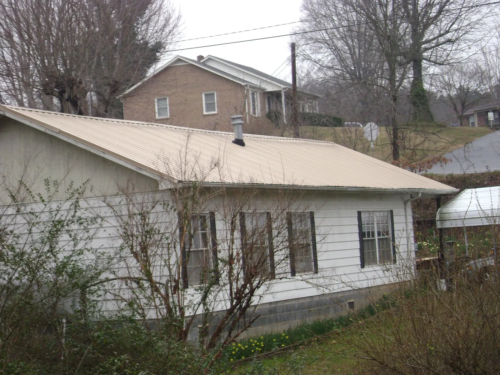 Tan metal roof on a white sided house set into a hillside — Commercial Roofing by Roofing Brothers in Savona