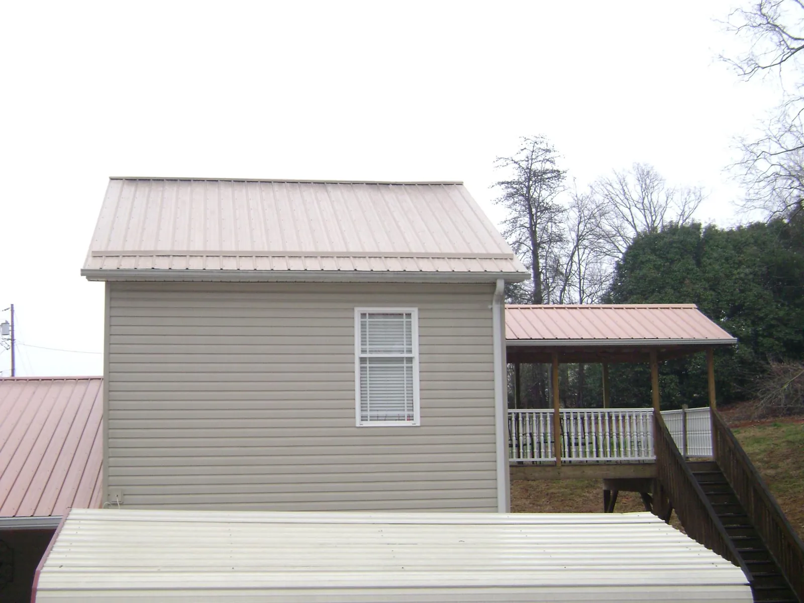 Tan metal roofs on a two story addition and attached porch, from a Roof Replacement job in Savona